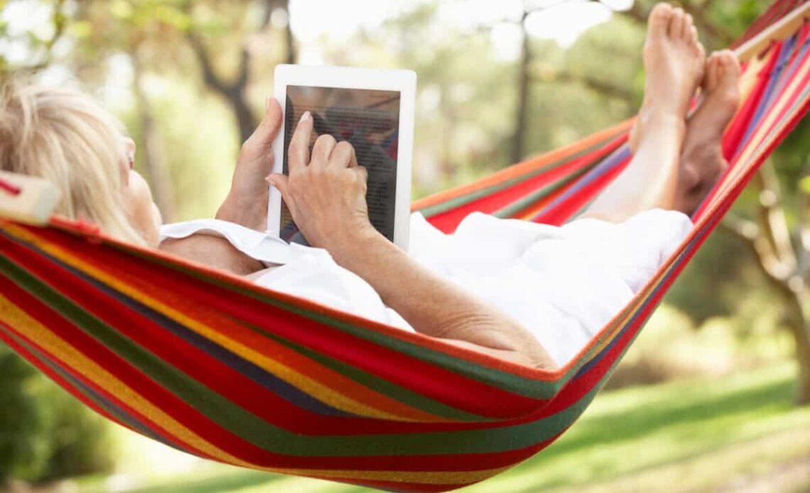 senior relaxes in hammock with e-book